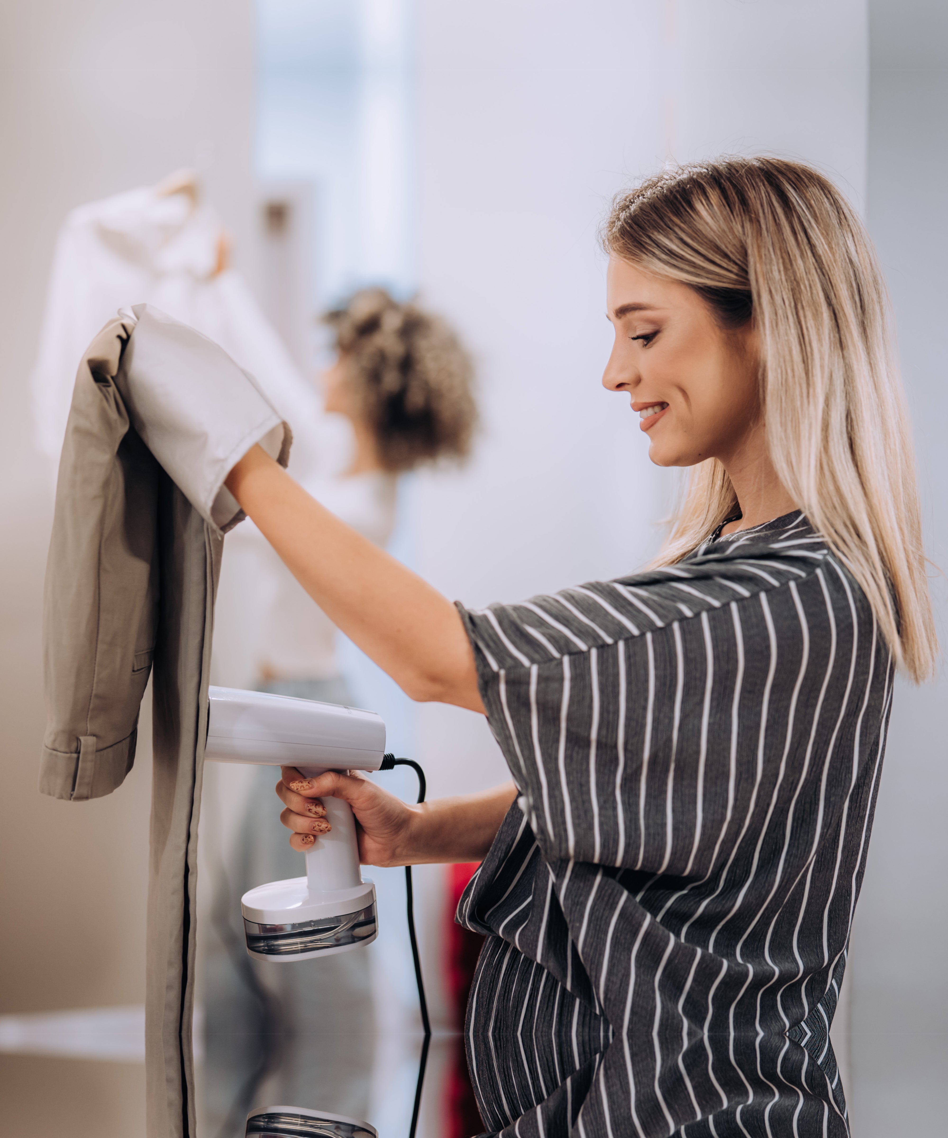 Blonde vrouw stoomt kleding met de FLOWSTEAM Kledingstomer